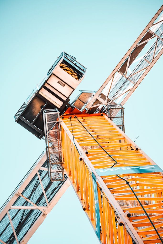 A striking low angle shot of a vibrant yellow tower crane against a clear sky, showcasing industrial power.